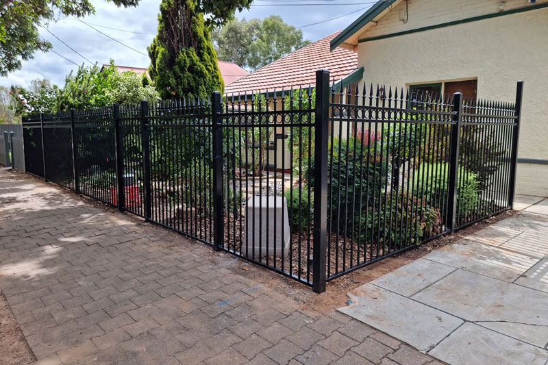 About-Us-home Black tubular fence around a front garden beside a paved path