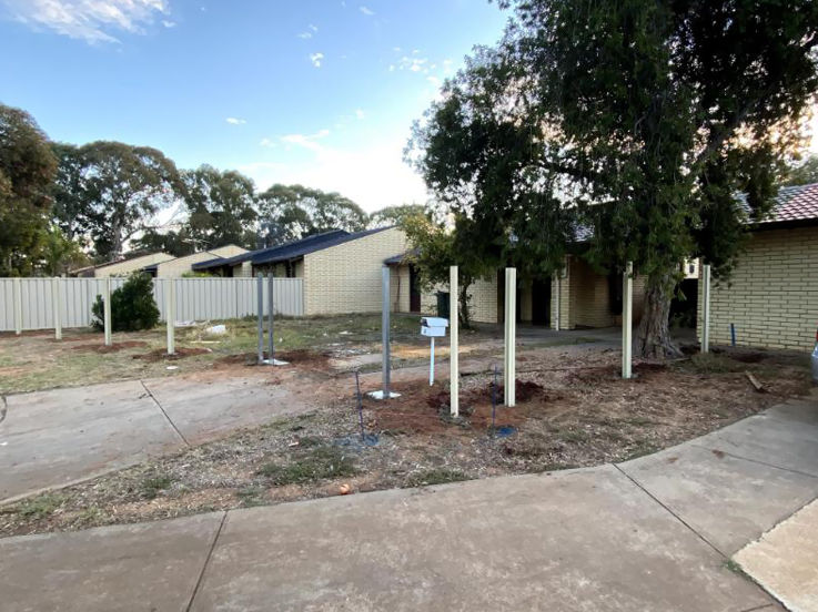 Cream fence posts standing in a front yard beside brick units
