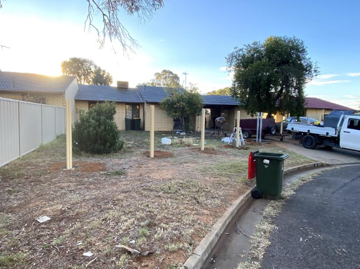 Fence posts set in a front yard beside a cream fence and a ute