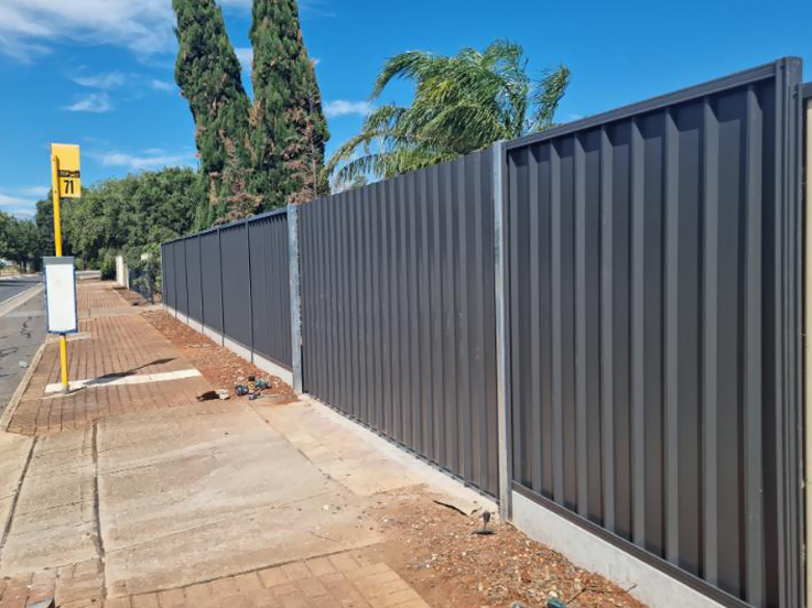 Long dark steel fence along a street footpath near a bus stop