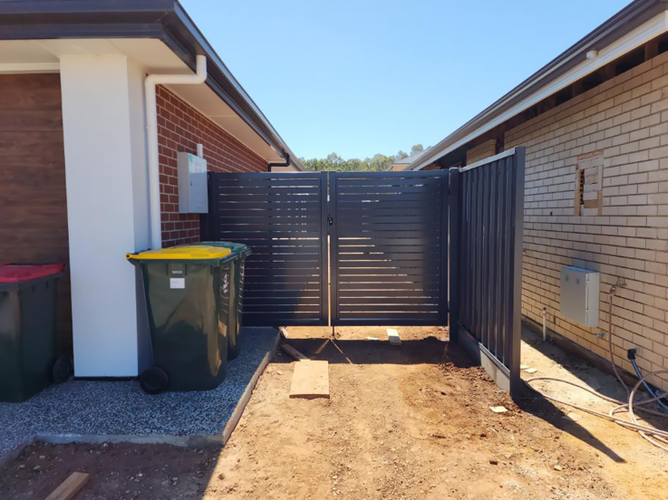 Dark slatted double gates and fence between two brick homes