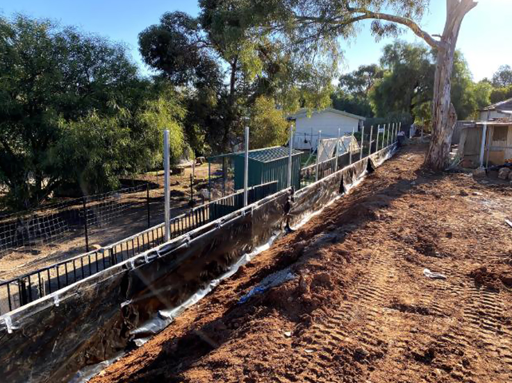 Black tubular fence on a new retaining wall beside an excavated slope