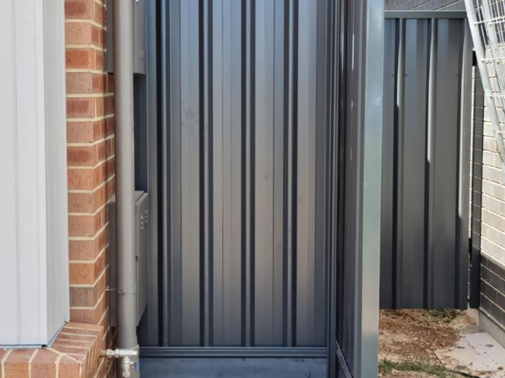Close-up of a dark steel fence panel beside a brick wall