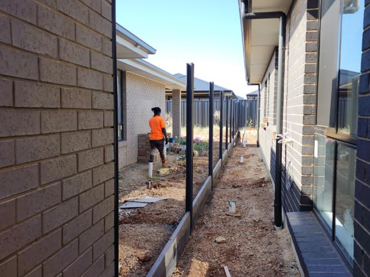 Worker in hi-vis setting black fence posts beside new brick homes