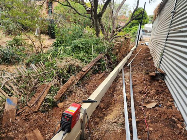 Retaining wall posts and sleepers going in beside a corrugated steel fence