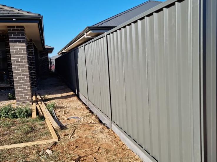 Grey-green steel side fence running beside a brick home