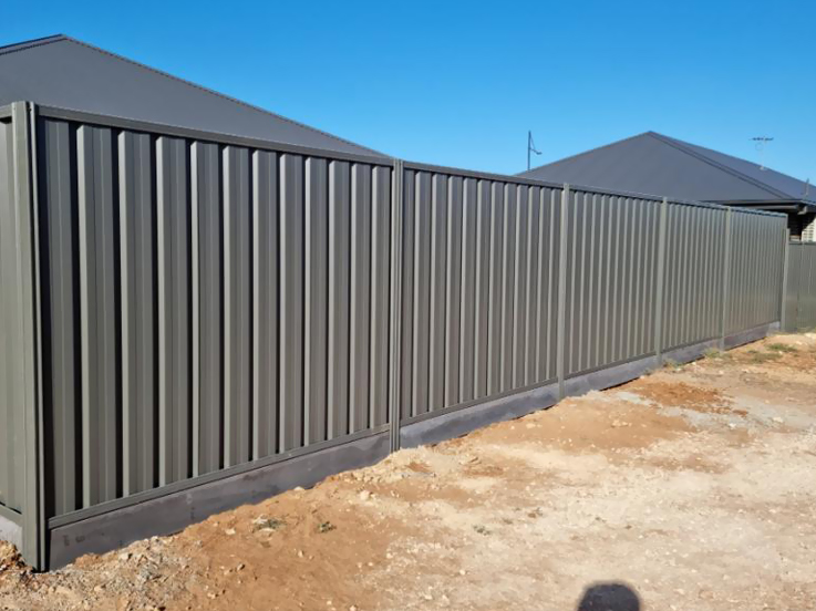Grey-green steel fence along a new home's dirt backyard