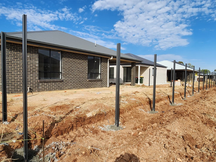 Black steel fence posts set in a trench beside a brick home
