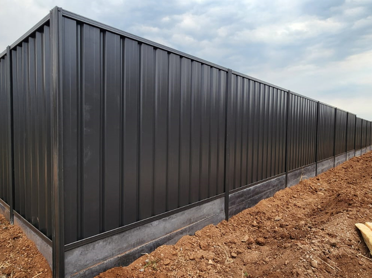 Long dark corrugated steel fence with a plinth along fresh soil