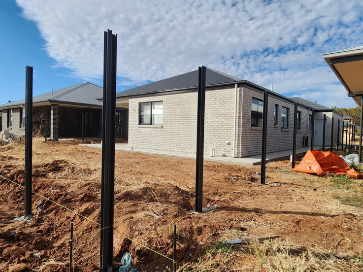 Black steel fence posts and a string line in a trench beside new homes