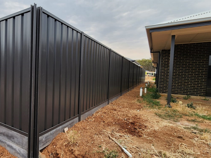 Dark corrugated steel side fence running past a brick home