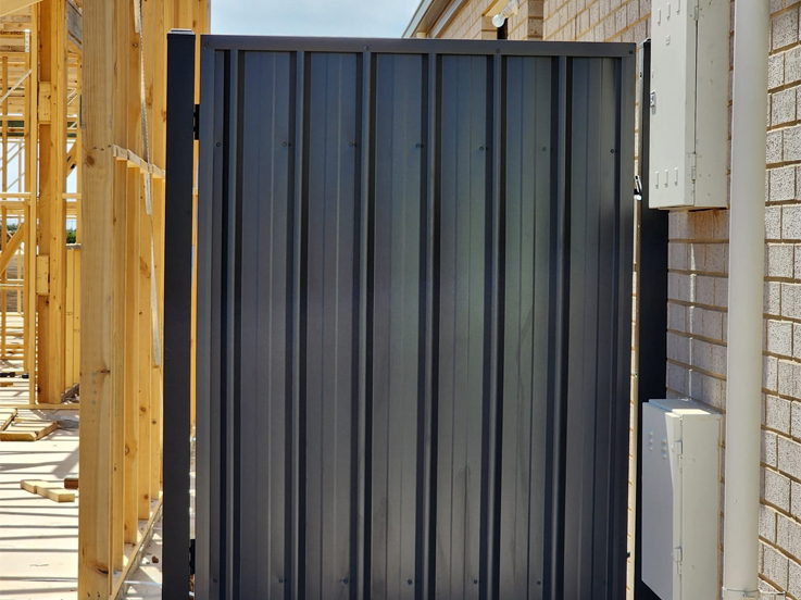 Dark steel side gate next to a house frame under construction