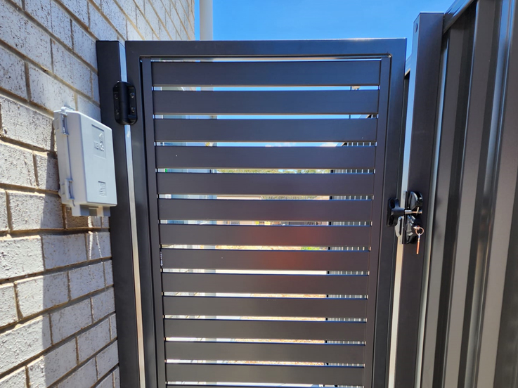 Grey slatted side gate with a lock between brick walls