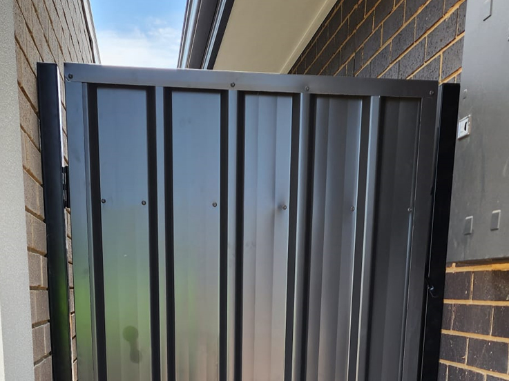 Close-up of a dark steel side gate against a brick wall