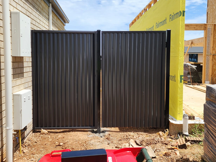 Dark steel double gates beside a house under construction
