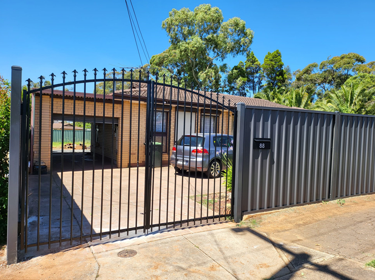 Black arched tubular driveway gates beside a dark steel fence