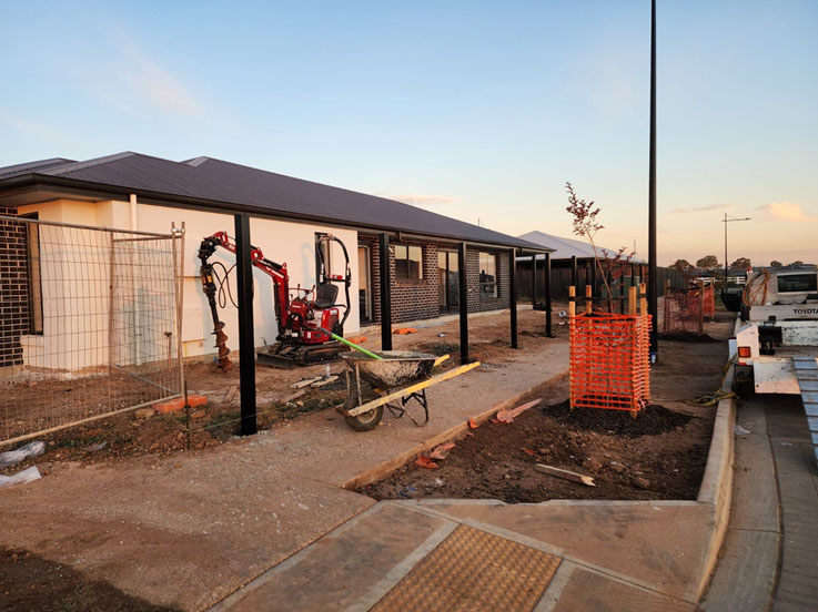 Mini excavator and black steel fence posts in front of a new house