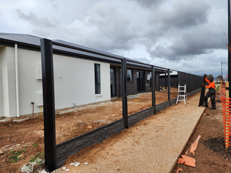 Worker installing black steel fence frames with plinths along new homes