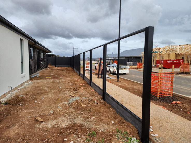 Black steel fence posts and rails beside a footpath and new house