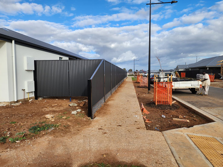 Dark corrugated steel fence wrapping the corner of a new home's yard