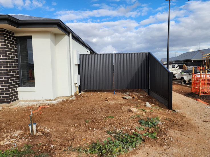 Dark corrugated steel fence along the side of a new brick home