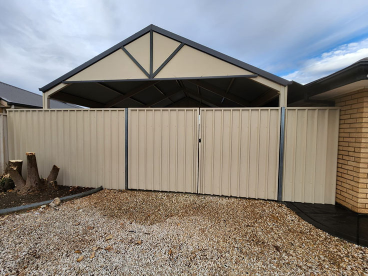 Cream steel fence with double gates closed in front of a carport